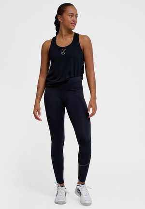 Svart sports tank topp med et chevron-mønster, kombinert med høyhåndt svarte leggings som har en subtil stripe. Hvide sportsko.
