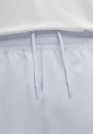 Nahaufnahme von hellgrauen Sweatpants mit elastischem Bund, in die ein weißes, geripptes Oberteil gesteckt ist, wobei die Enden der Kordelzugmitte über der Naht sichtbar sind.