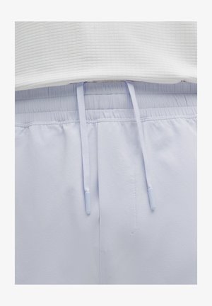 Close-up van lichtgrijze elastische tailleband trainingsbroeken met een wit geribbeld topje erin gestopt, waarbij de uiteinden van het trekkoord in het midden boven de naad zichtbaar zijn.