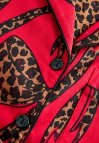 Punane kangas, millel on leopardimustriga mustrid ja mustad aktsendid. Sisaldab ümarat kraed ja ees musta nööbiga detaili.