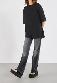 Sort oversized t-shirt med korte ærmer, parret med slidte grå flared jeans og sorte platform sandaler. Minimalistisk urban stil.
