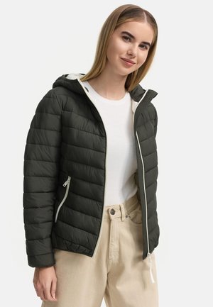 Mörkgrön vadderad jacka med huva, vit dragkedja och foder, med diagonala sömmar. Kombinerad med en vit topp och beige byxor.