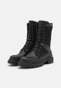 Botas de combate negras que presentan una mezcla de materiales de cuero y ante, con un caña alta, cordones en la parte frontal, suela resistente y puntera reforzada.