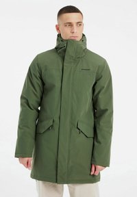 Manteau imperméable vert avec un col haut, fermeture éclair à l'avant et deux poches inclinées. Fabriqué en tissu lisse avec un design minimaliste.