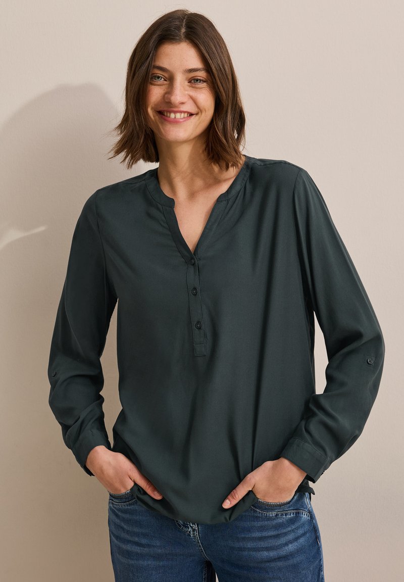 Blusa a maniche lunghe verde scuro con colletto arrotondato, apertura con bottoni e vestibilità comoda. Presenta una texture liscia e polsini arrotolati.