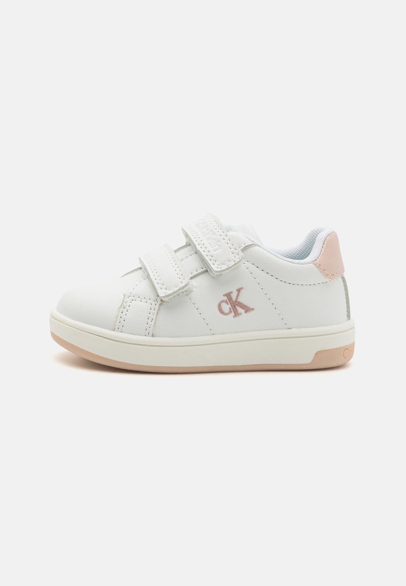 Baskets synthétiques blanches avec deux sangles Velcro, accents rose clair au niveau du talon, et une semelle en caoutchouc arborant un logo discret.