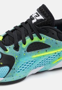 Sneaker med en sort overdel og lyseblå accenter. Designet har et struktureret mønster med neongrønne sprøjt og netdetaljer.