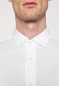 Biała bawełniana koszula z kołnierzykiem na guziki, charakteryzująca się gładką fakturą i klasycznym krojem, z pięcioma guzikami z przodu.