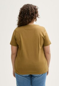 Mosterdgele t-shirt met korte mouwen van zachte stof, met een ronde hals en een relaxte pasvorm, gecombineerd met lichtblauwe jeans.