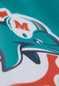 Tissu turquoise présentant un logo des Miami Dolphins avec des accents blancs et orange. Texture lisse avec des lignes distinctes et des couleurs vives.