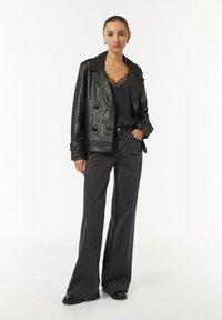 Schwarze Leder-Doppelreiherjacke über einem schwarzen, mit Spitze besetzten Oberteil. Flared schwarze Hosen mit silbernen Sprenkeln und klobigen schwarzen Stiefeln.