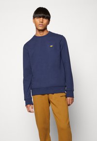 Navy blue sweatshirt made of soft fabric, featuring a crew neck and ribbed cuffs. Notable small embroidered design on the chest.