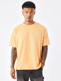 Overmaatse oranje katoenen t-shirt met een ronde hals en een wit hartontwerp. Heeft korte mouwen en een zachte textuur.