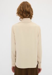 Helle beige Bluse mit langen Ärmeln und Kragen, ausgestattet mit geknöpften Manschetten und einer glatten Stoffstruktur, im geraden Schnitt gestaltet.