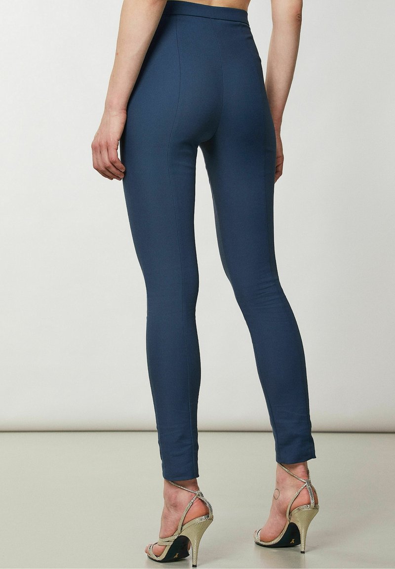 Marinblå leggings med hög midja, slät textur och åtsittande design. Bärs med metalliska klackar med remmar, vilket visar vristen.