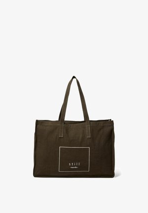 Tummanvihreä kankainen olkalaukku, jossa on kaksi vankkaa kahvaa ja valkoinen painettu logo suorassa kehykssä. Yksinkertainen, käytännöllinen muotoilu.