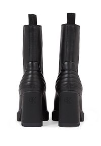 Czarne skórzane botki za kostkę z żebrowaną fakturą z tyłu i masywnymi kwadratowymi obcasami. Posiadają pętle na górze, ułatwiające zakładanie.
