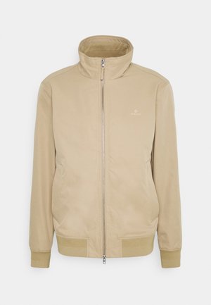 Beige Jacke mit hohem Kragen, frontalem Reißverschluss und gerippten Bündchen. Verfügt über seitliche Taschen und eine dezente Markenkennzeichnung auf der Brust. Glatte Textur.
