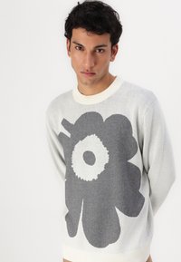 Hellgrauer Pullover mit einem großen dunkelgrauen floralen Muster, geripptem Rundhalsausschnitt und strukturiertem Strickstoff.