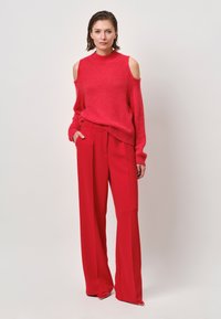 Rode off-shoulder trui gecombineerd met hoge taille rode wijde broek. Zachte textuur, levendige kleur en een nauwsluitende pasvorm met zakken.