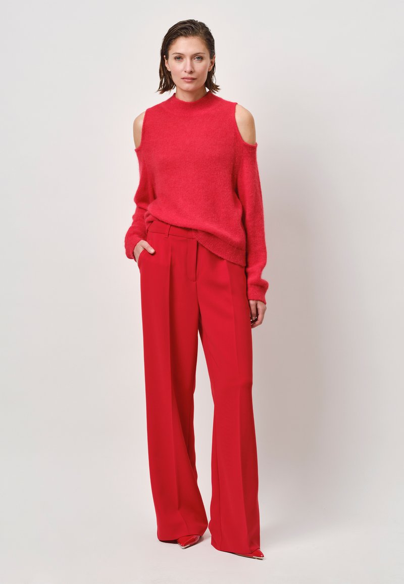 Rode off-shoulder trui gecombineerd met hoge taille rode wijde broek. Zachte textuur, levendige kleur en een nauwsluitende pasvorm met zakken.