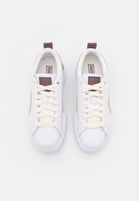 Fehér tornacipő bézs részletekkel, sima bőr felső résszel, kerek orral, krémszínű fűzővel és hátul található hurkával a könnyű felhúzás érdekében.