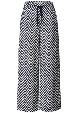 Gros plan d'une personne portant un pantalon à motif zigzag bleu marine et blanc avec un cordon de serrage et un haut de couleur claire.