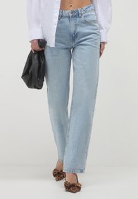 Jeans alti di vita blu chiaro con vestibilità dritta, caratterizzati da un leggero sbiadimento e un classico design a cinque tasche, abbinati a una borsa nera.