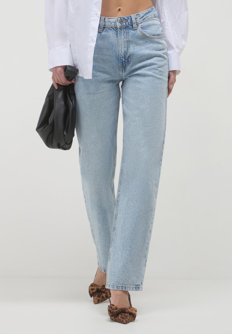 Jeans alti di vita blu chiaro con vestibilità dritta, caratterizzati da un leggero sbiadimento e un classico design a cinque tasche, abbinati a una borsa nera.