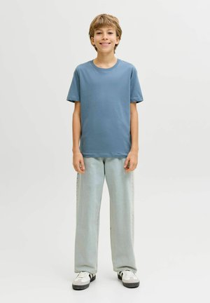 Lichtblauw katoenen T-shirt met korte mouwen, gecombineerd met lichtgroene wijde jeans. Schoeisel heeft een mix van witte en grijze kleuren.