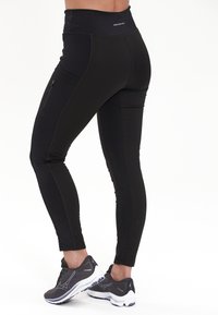 Mustat urheilulegginsit korkealla vyötäröllä, sivutaskulla ja tiukalla muotoilulla. Silkkinen pinta, vahvistetut saumat ja ilman näkyviä kuvioita.