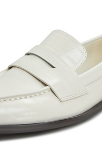 Weißer Lederloafer mit strukturierten Oberflächen, ausgestattet mit einem breiten Riemen über dem Blatt und kontrastierenden Nähten. Abgerundete Zehenpartie und flache Sohle.