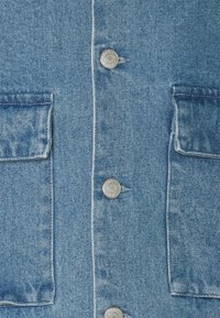 Light blue denim jacket front with two flap pockets and silver metal buttons down the center.