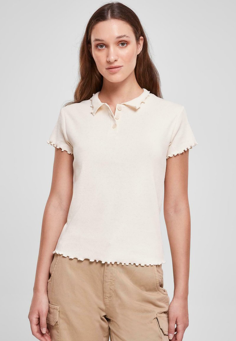 Cremefarvet ribbet polo skjorte med bølget krave og korte ærmer, featuring tre knapper ved halsen og en cropped kant.