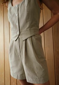 Khaki linnebyxdress med en figurnära överdel, rundad halsringning och stora vita knappar. Har plisserade shorts och en texturerad finish.