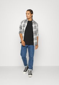Svart t-skjorte kombinert med en hvit og svart rutete skjorte med knapper, blå denimjeans og svarte høyhælte sneakers med hvite såler.