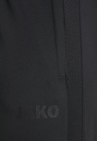 Schwarze Sportshorts mit strukturierten Mesh-Seitenpanelen und glattem Stoff. "JAKO"-Logo in glänzender Ausführung auf der Vorderseite aufgedruckt.