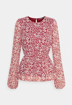 Blusa floreale rossa con maniche lunghe e trasparenti, vita arricciata, scollatura rotonda e piccolo dettaglio a chiave sulla schiena. Presenta fiori bianchi e arancioni.