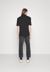 Tricou polo negru cu mânecă scurtă asociat cu pantaloni gri închis. Materialul pare neted, cu o croială clasică și un design simplu. Pantofi casual incluși.