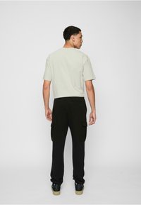 Light grey short-sleeve t-shirt paired with black cargo pants featuring side pockets and elastic cuffs, viewed from the back.