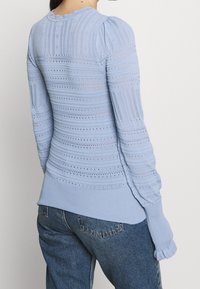 Hellblauer Strickpullover mit strukturierten Mustern, gerippten Bündchen und einer taillierten Passform, mit verlängerten Ärmeln und leichtem Stretch.