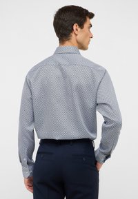Camicia con bottoni caratterizzata da un motivo geometrico blu e bianco, realizzata in tessuto leggero con colletto standard e maniche lunghe.