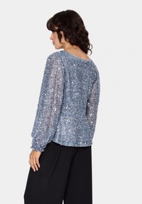 Lys blå sequinned blouse med lange ærmer, let løs pasform, rund halsudskæring, struktureret stof, parret med sorte brede bukser.