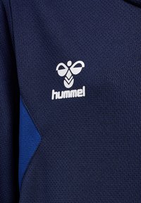Mørkeblå sports T-shirt med en tekstureret stof, der har en hvid "hummel"-logo og geometriske blå accenter på siderne.