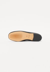 Semelle de chaussure noire avec une surface texturée, dotée d'un fond en caoutchouc marron clair et d'un logo de marque embossé. Fini lisse avec des rainures pour l'adhérence.