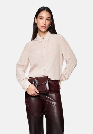 Beige long-sleeve shirt with button front, worn with glossy burgundy faux leather pants and a small matching handbag featuring a silver clasp.