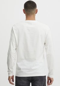 Langærmet hvid bomulds T-shirt med rund hals og afslappet pasform, der har en glat tekstur og minimal syning ved halsudskæringen.