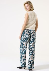 Top sans manches en tricot crème associé à un pantalon large teal présentant un motif floral et des motifs paisley avec des accents blancs, rouges et bleus.