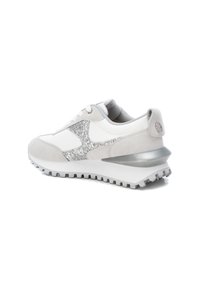 Vit och ljusgrå sportskor med glittrig silverdetalj på sidan, kraftig sula, snörning och vadderad krage, visad från bakre högra sidan.