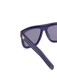 Mörkblå solglasögon med geometrisk design, mörka linser och metallaccenter som har en guldlogotyp på skalmen.